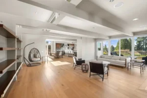 Modern great room with hardwood floors, exposed beams, a hanging egg chair, and large glass doors to a back garden.